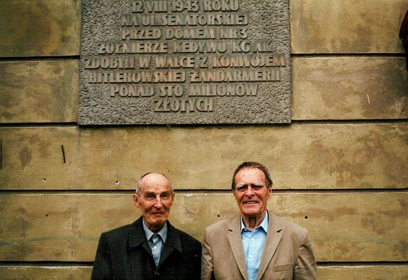 Uczestnicy akcji „Góral” Tadeusz (z lewej) i Andrzej Żupańscy pod tablicą pamiątkową w miejscu napadu (fot.: Zupan60; lic. CC ASA 3.0).