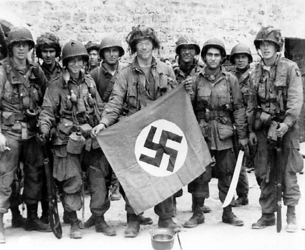 Amerykańscy spadochroniarze ze 101 Dywizji Powietrznodesantowej w pierwszych dniach inwazji w Normandii. Na pierwszym planie James Flanagan ze zdobytą nazistowską flagą w rękach (fot. U.S. Army, domena publiczna).