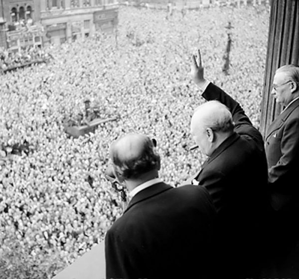 Winston Churchill pozdrawia tłumy z jednego z budynków rządowych na ulicy Whitehall (fot. domena publiczna).
