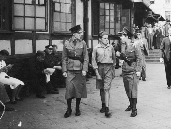 Policjantki prowadzą młodego kieszonkowca do izby zatrzymań ulicami Warszawy roku 1939 (źródło: domena publiczna).